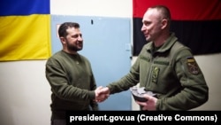 Pe 23 martie, militarii din regiunea Herson i-au oferit președintelui Volodimir Zelenski (stânga) un ceas confecționat dintr-un tun inamic avariat pe a cărui carcasă este reprezentată harta Crimeei