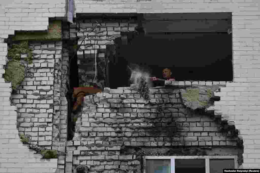 Un localnic curăță molozul din apartament după ce blocul în care stă a fost lovit de fragmente de rachete rusești.