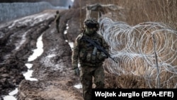 La granița dintre Polonia și Belarus, în apropiere de satul Czeremcha, un militar patrulează în lungul barierei de sârmă ghimpată, 17 decembrie 2021.