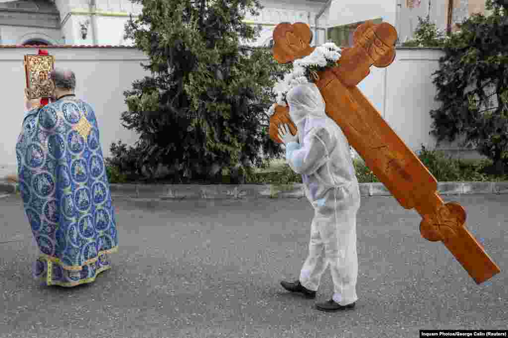Un credincios îmbrăcat în combinezon de protecție cară în spinare o cruce în cadrul unui ritual religios din București, cu ocazia Vinerei Mari, pe 17 aprilie. 
