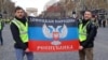 Флаг группировки «ДНР» во время протестов в столице Франции. Его держат: Фабрис Сорлин (слева) и Ксавье Моро