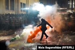Un polițist mascat lovește o fumigenă în fața parlamentului din Georgia, în a doua noapte de proteste (29 noiembrie) izbucnite după anunțul guvernului că va suspenda discuțiile de aderare la UE.