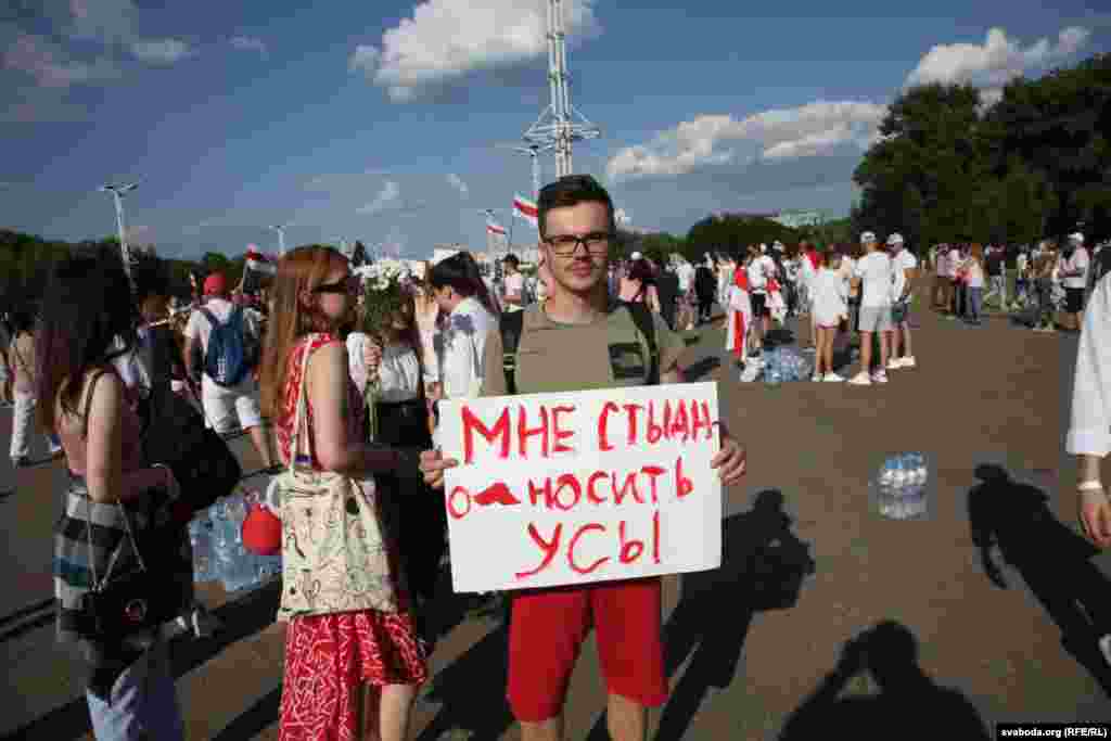 Un manifestant ține un banner pe care scrie : „Mi-e rușine să port o mustață”, făcând aluzie la podoaba facială a lui Lukașenka.