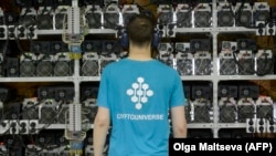 Egy alkalmazott szemrevételezi a bitcoin-bányászathoz használt gépeket a oroszországi Kirisiben található CryptoUniverse cégnél 2018. augusztus 20-án. A bitcoin és más kriptovaluták bányászatához nagy kapacitású számítógépekre és olcsó áramra van szükség.